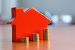 Varias columnas de monedas y una casa en miniatura sobre una mesa para explicar algo de vivienda muy difícil de entender